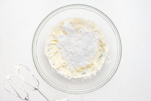 powdered sugar on top of whipped butter and cream cheese in glass bowl