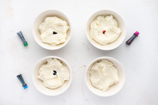 4 separate bowls with cream cheese mint mixture and dots of food coloring