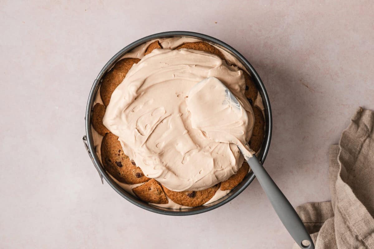 spatula spreading mocha whipped cream over cookies in springform pan