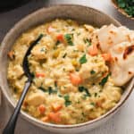 A bowl of mulligatawny soup with a piece of naan