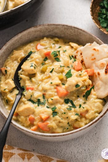 A bowl of mulligatawny soup with a piece of naan