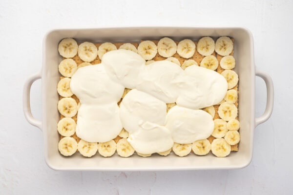 spoonfuls of pudding cream filling over sliced bananas in casserole dish