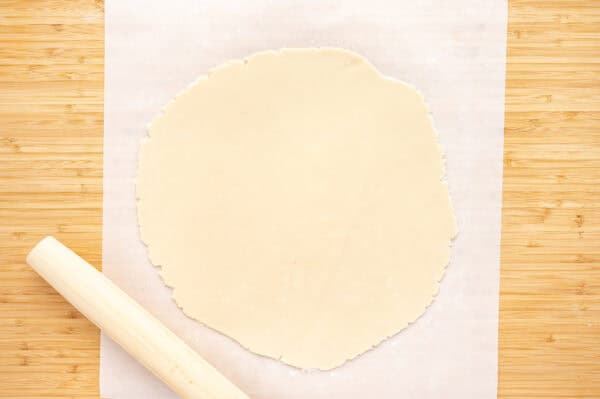 pie crust dough rolled out with rolling pin on parchment paper