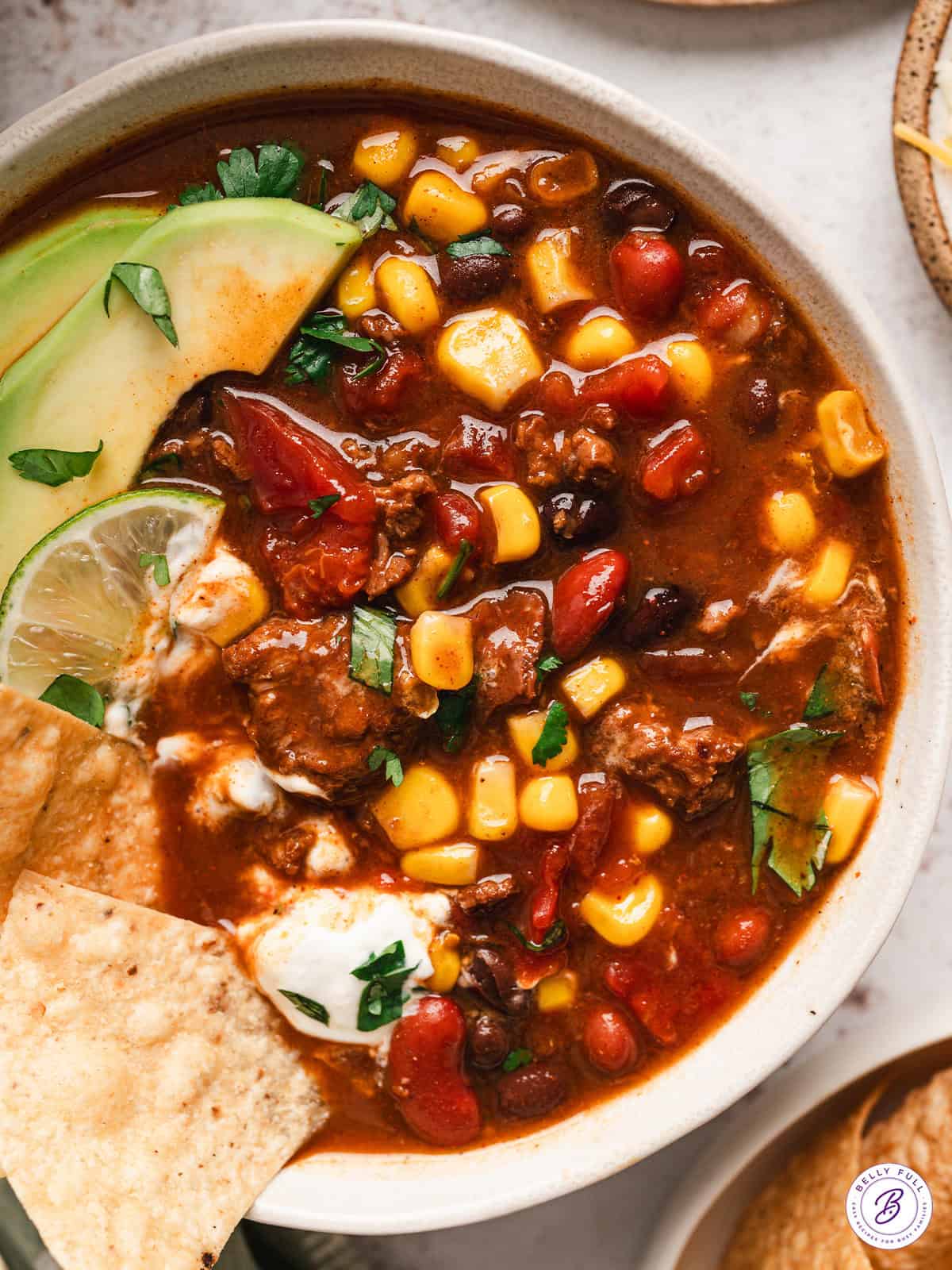 Overhead view of a bowl of 7 can soup with avocado slices, lime, and tortilla chips