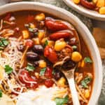 A spoon in a bowl of 7 can soup with shredded cheese, sour cream, and avocado slices