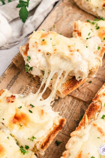 Pieces of chicken alfredo French bread pizza pulled apart with cheese stringing between them