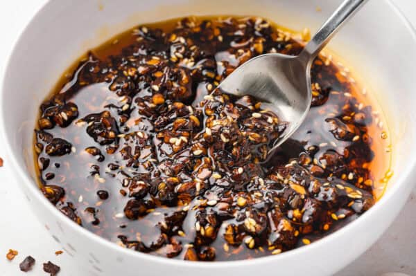 A spoon stirring homemade chili crisp in a white bowl