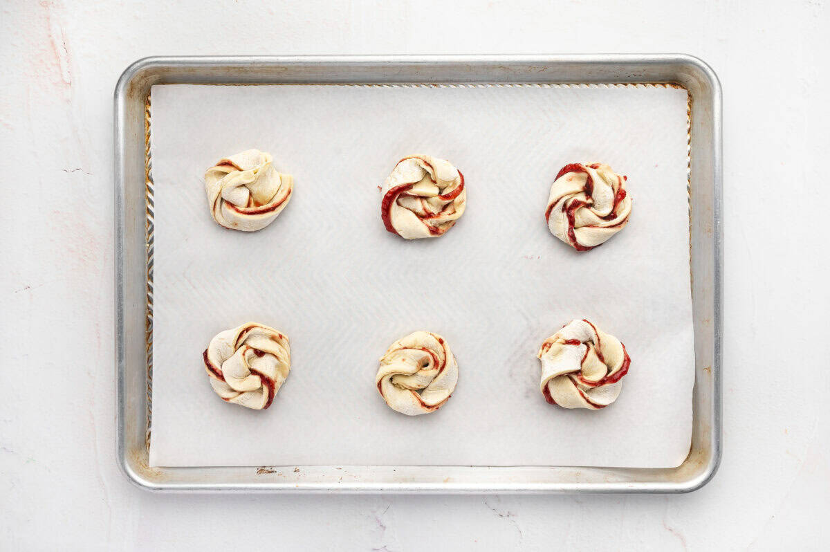 Unbaked jam puff pastry rolls on a baking sheet