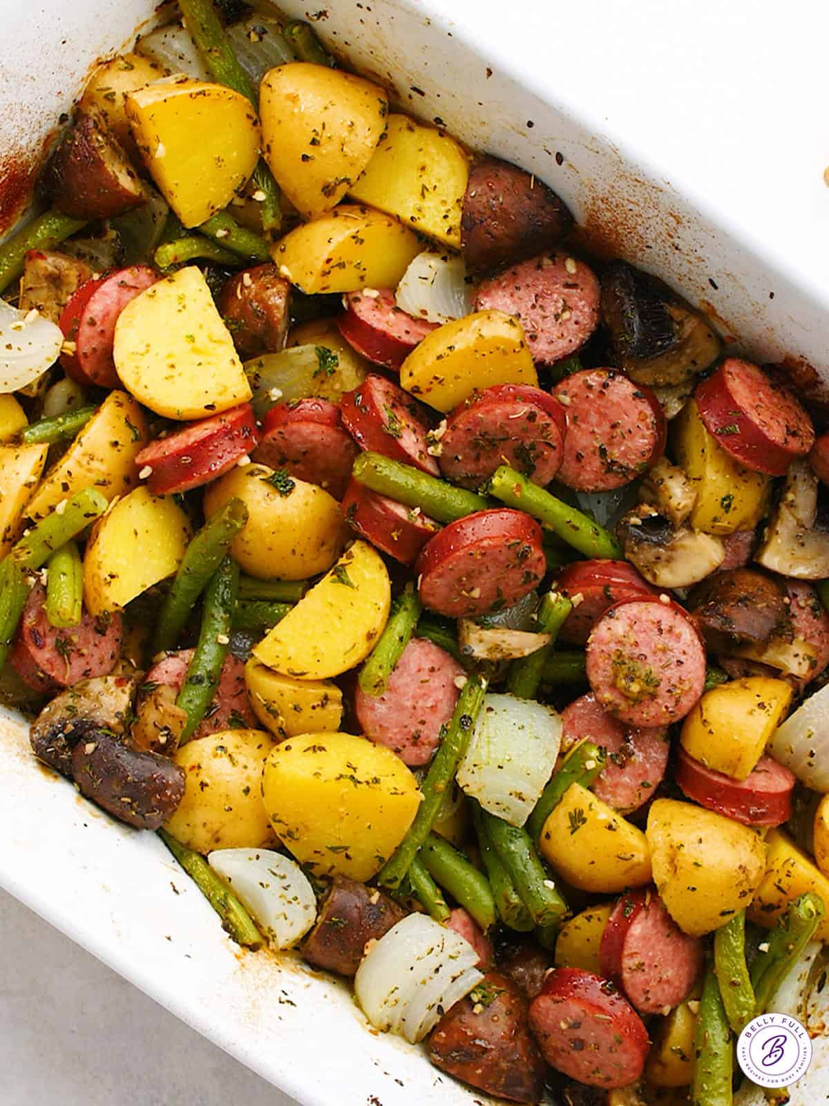 overhead baked sliced kielbasa, mushrooms, onion, and green beans in casserole dish