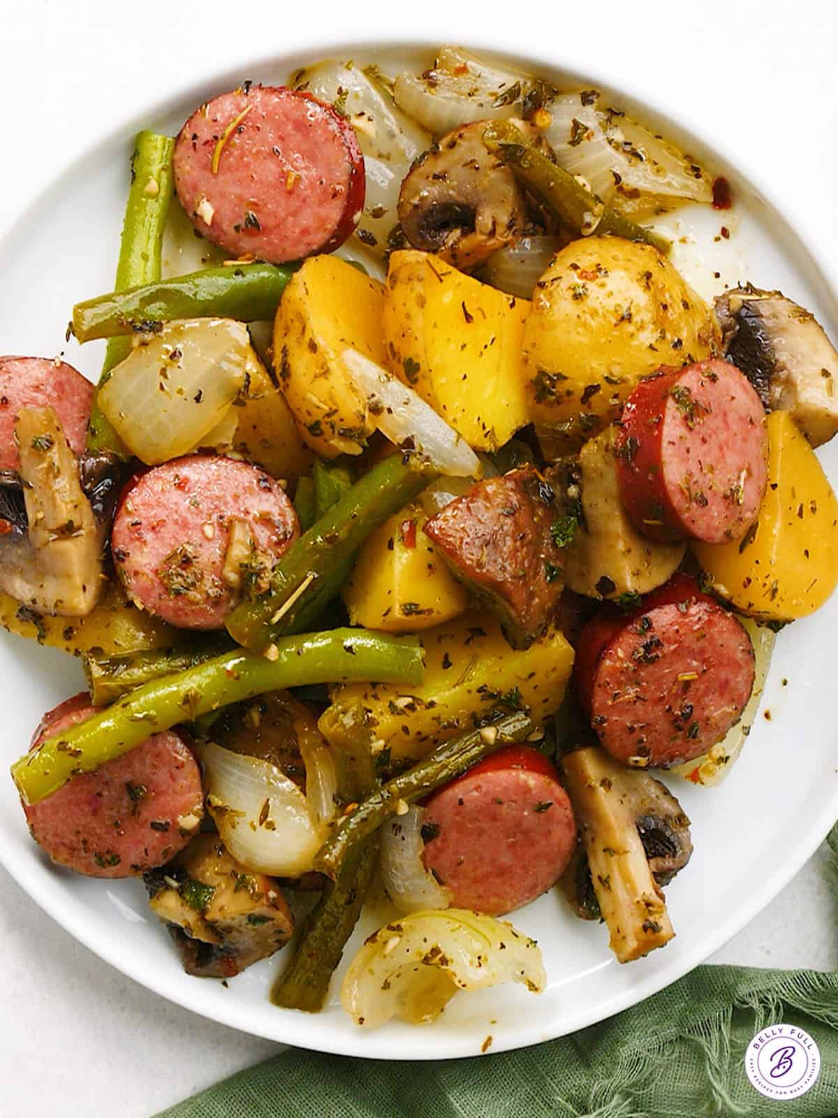 overhead baked sliced kielbasa, mushrooms, onion, and green beans on plate