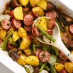 overhead baked sliced kielbasa and vegetables in casserole dish and serving spoon