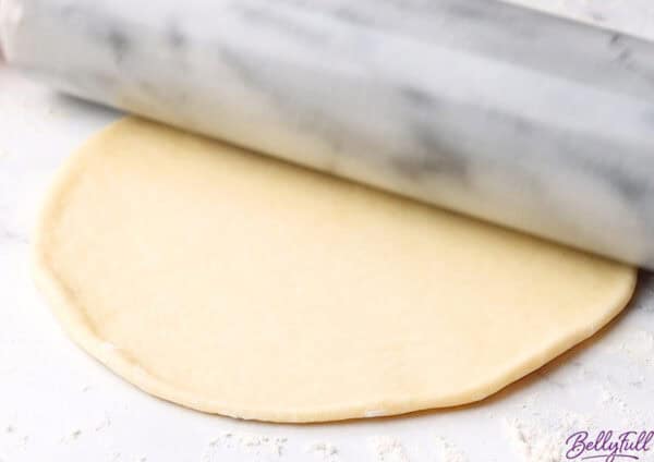 uncooked naan being rolled flat with rolling pin