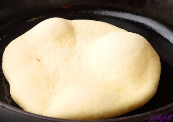 uncooked naan in skillet with bubbles