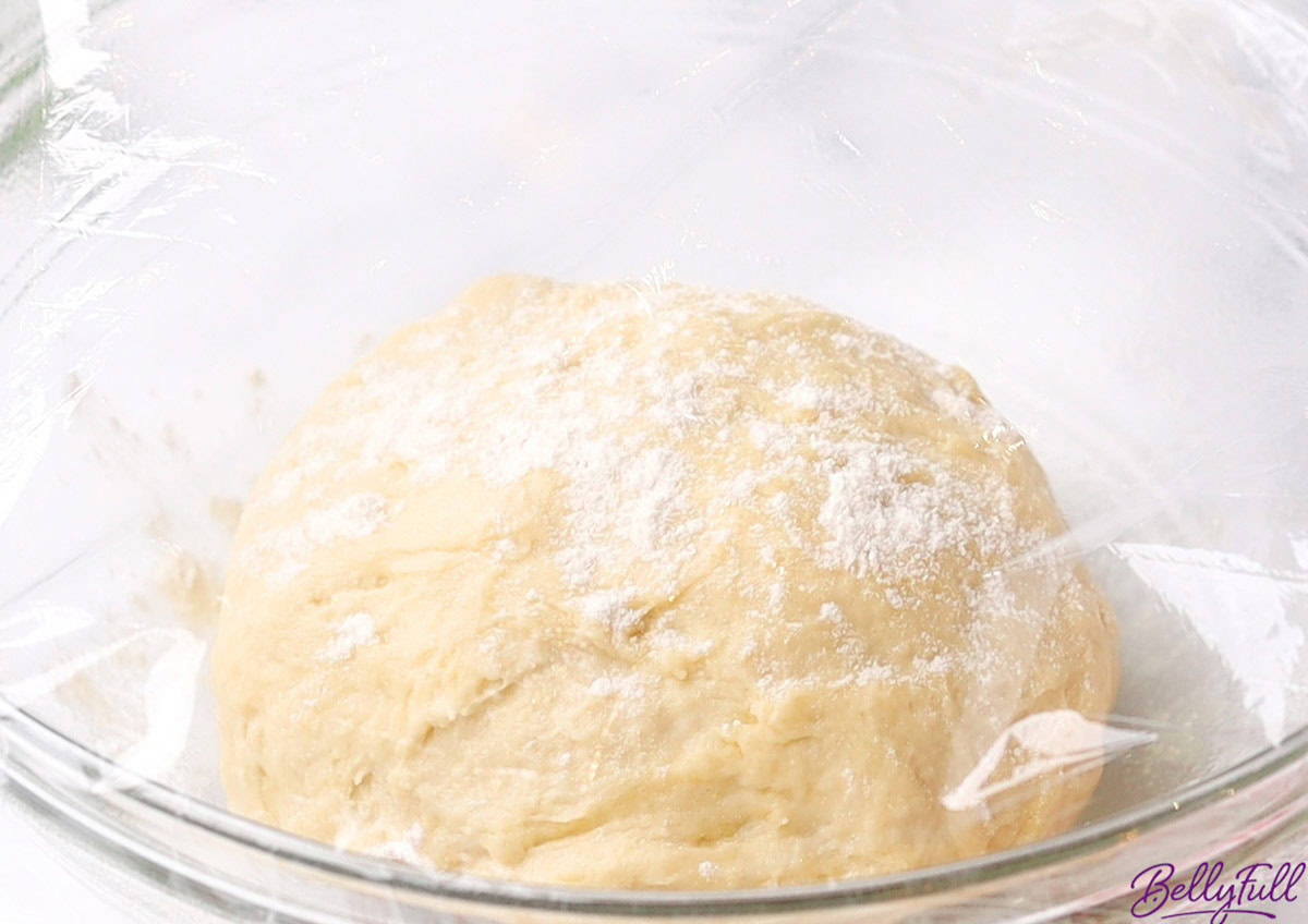 risen dough in bowl covered with plastic wrap