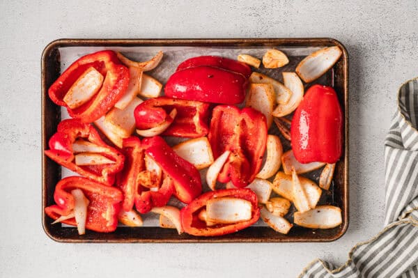 Overhead view of seasoned, quartered red bell pepper and sweet onion on a baking sheet.