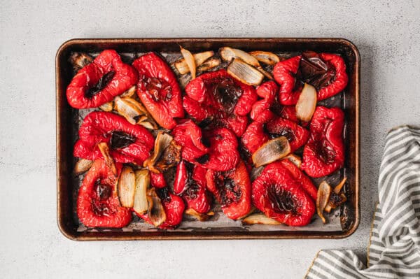 Overhead view of roasted, quartered red bell pepper and sweet onion on a baking sheet.