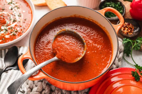 Roasted red pepper soup in a pot with a serving spoon.