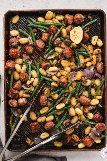 Tongs on a sheet pan of sausage and gnocchi