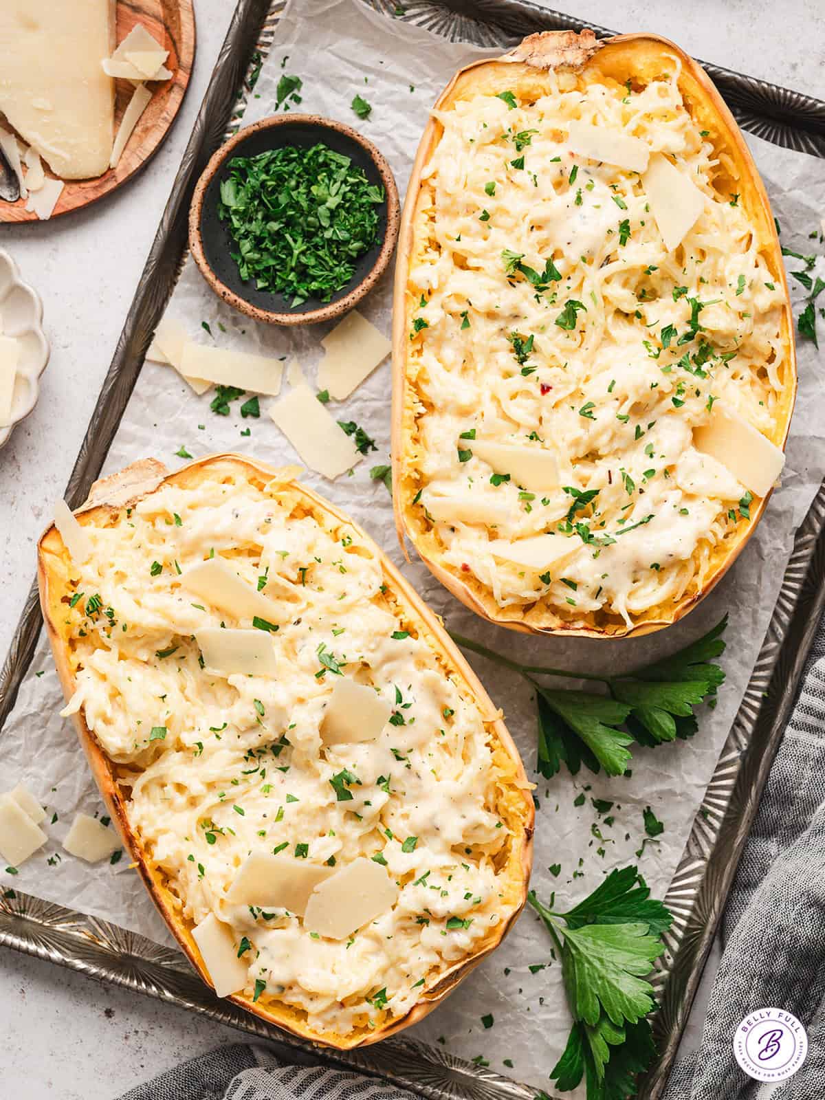 2 halves of spaghetti squash alfredo on baking sheet, garnished with parsley