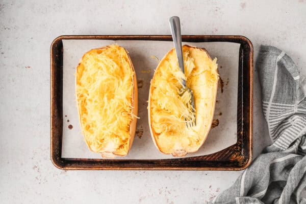 2 roasted halves of spaghetti squash on baking sheet with fork