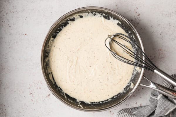 homemade alfredo sauce in pan with whisk