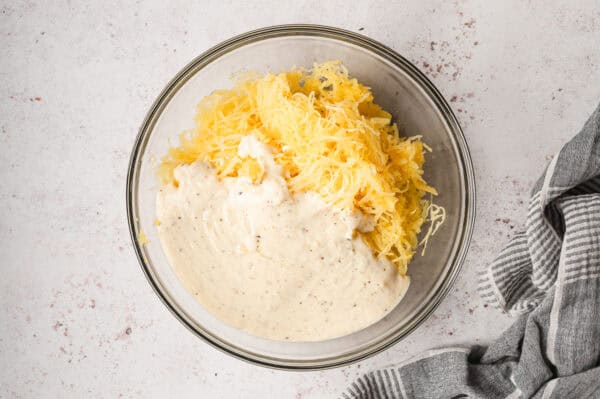 roasted spaghetti squash strands with alfredo sauce separate in glass mixing bowl