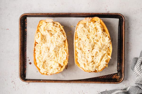 2 roasted halves of spaghetti squash stuffed with alfredo sauce on baking sheet