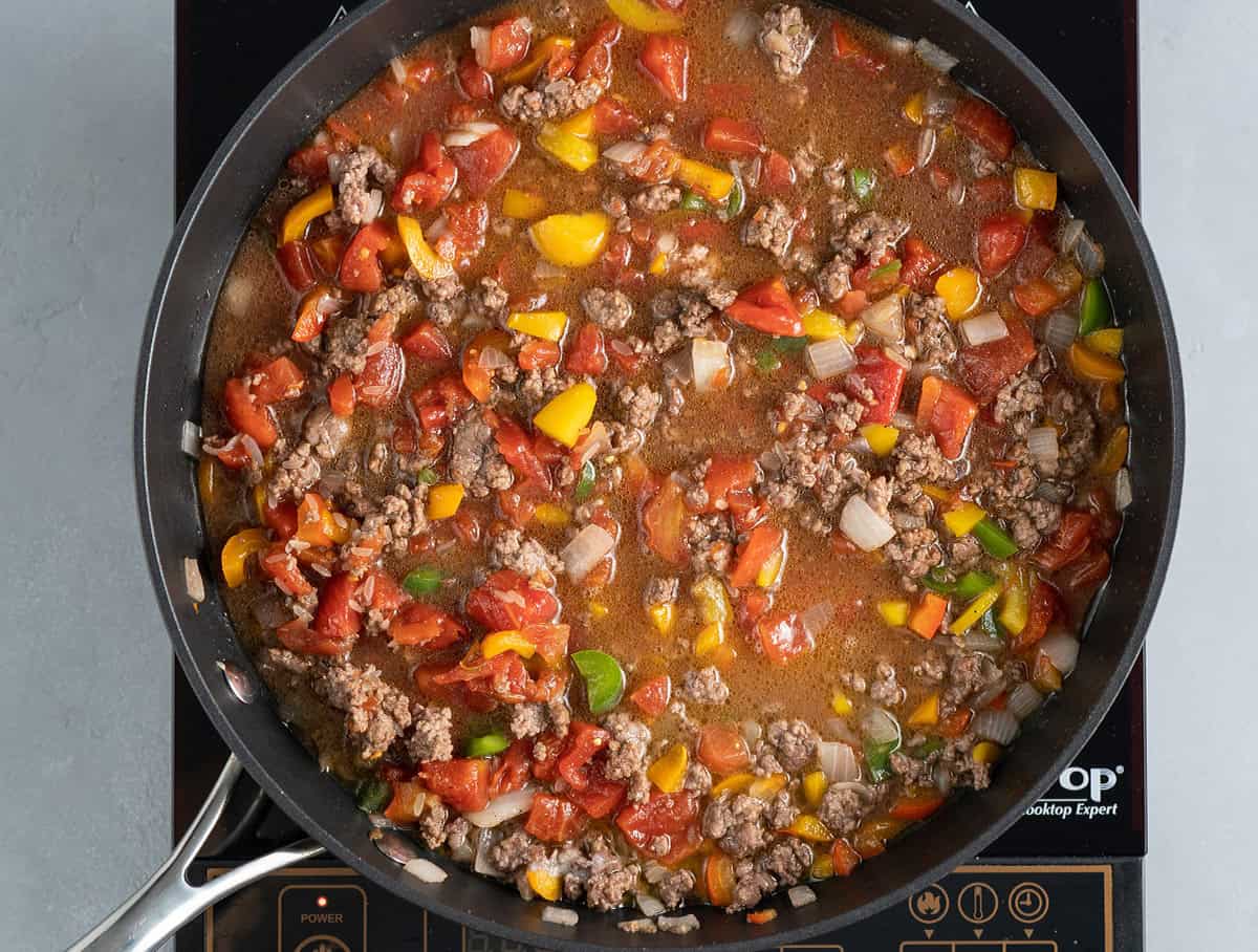 stuffed peppers filling with broth simmering in skillet