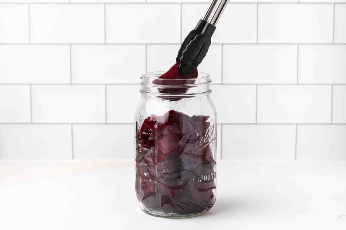 sliced beets being put in jar with tongs