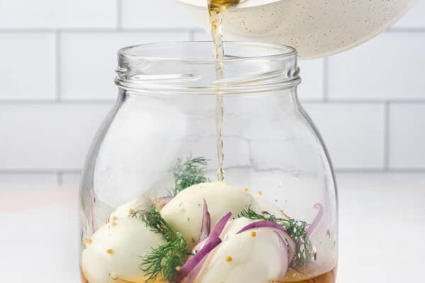 brine being poured over hard boiled eggs in jar