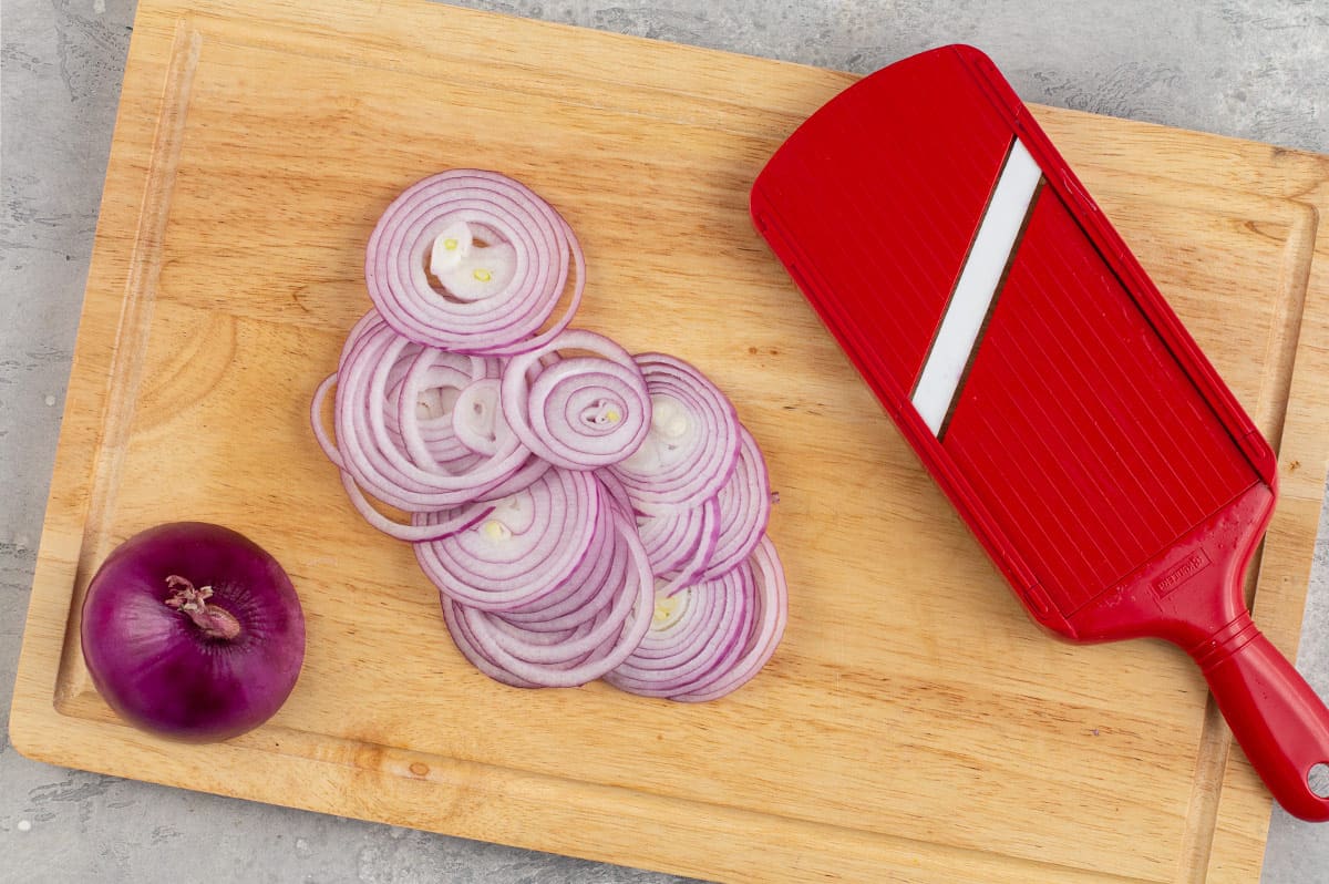 sliced red onion on cutting board with mandolin