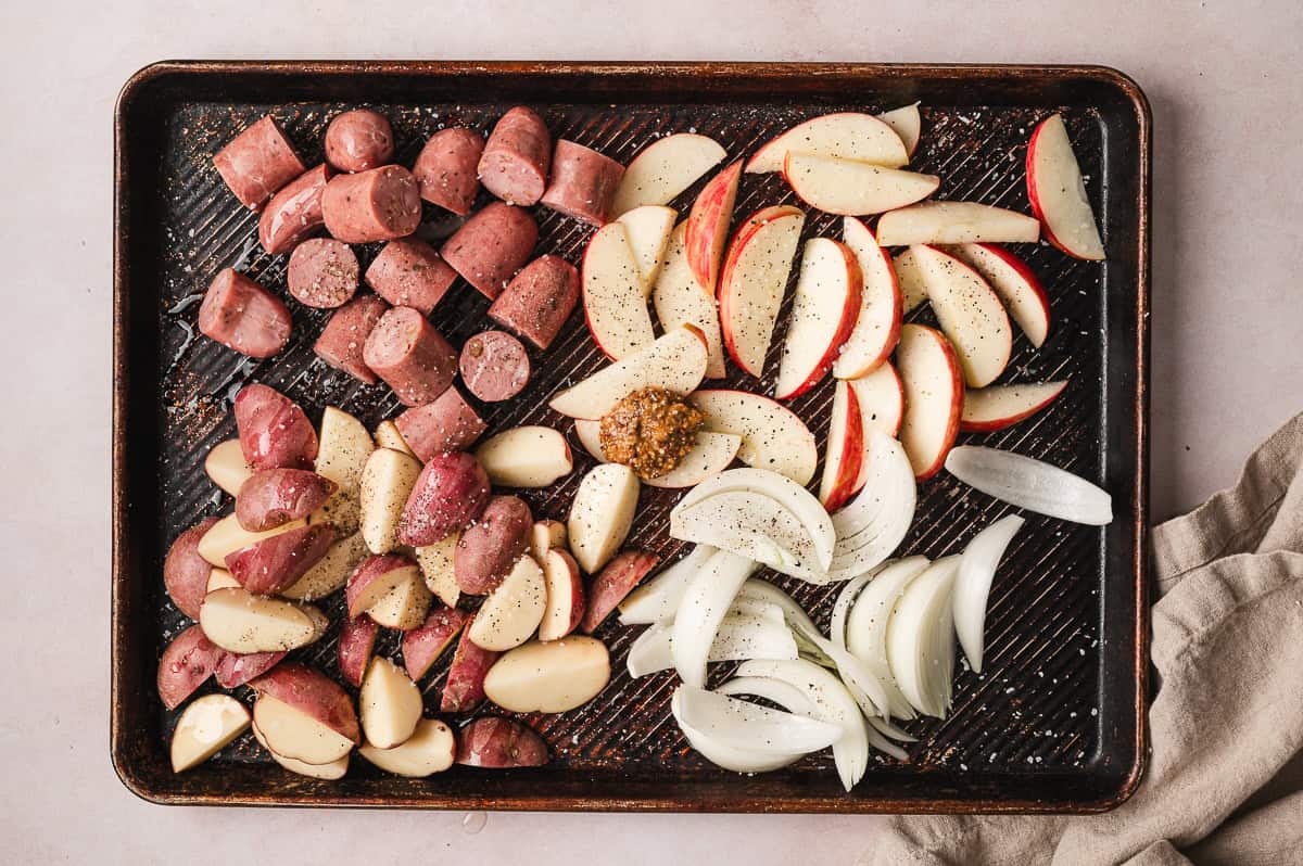 Chicken sausage, potatoes, apples, and onion on a baking sheet