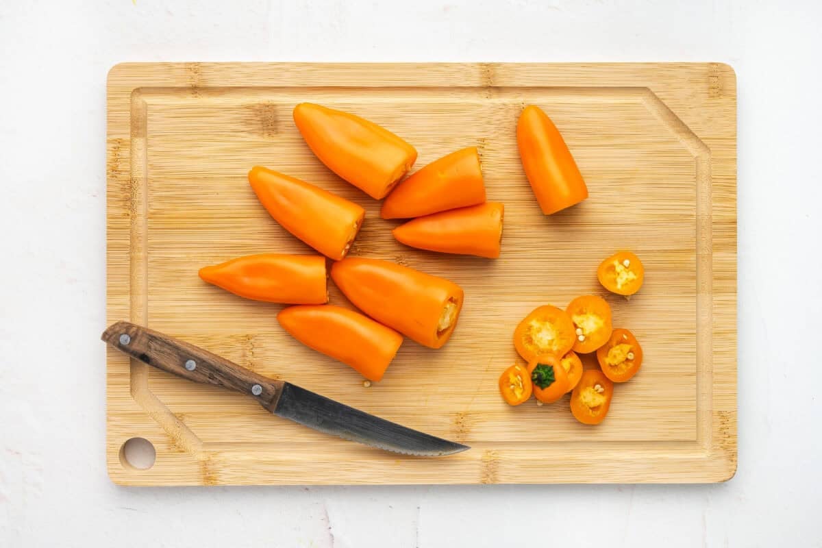 Orange mini peppers on a cutting board with the tops cut off