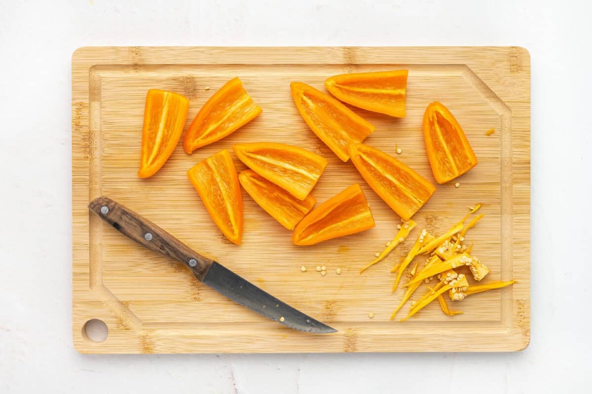 Orange mini bell peppers cut in half on a cutting board
