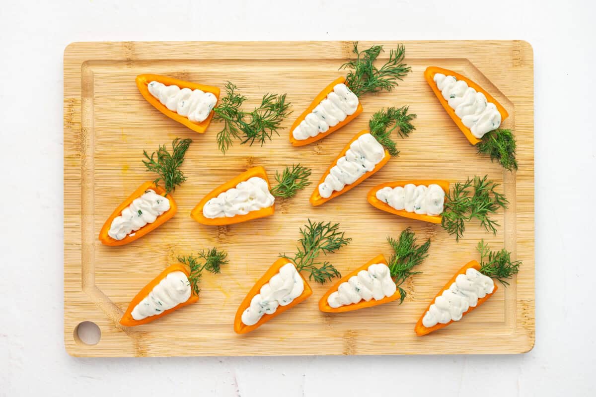 Orange mini bell peppers stuffed with a cream cheese mixture on a cutting board