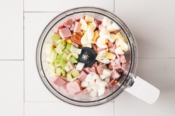 chopped ham, celery, onion, and hard boiled eggs in bowl of food processor
