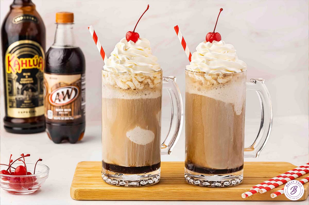 Two boozy root beer floats in mugs topped with whipped cream and a cherry