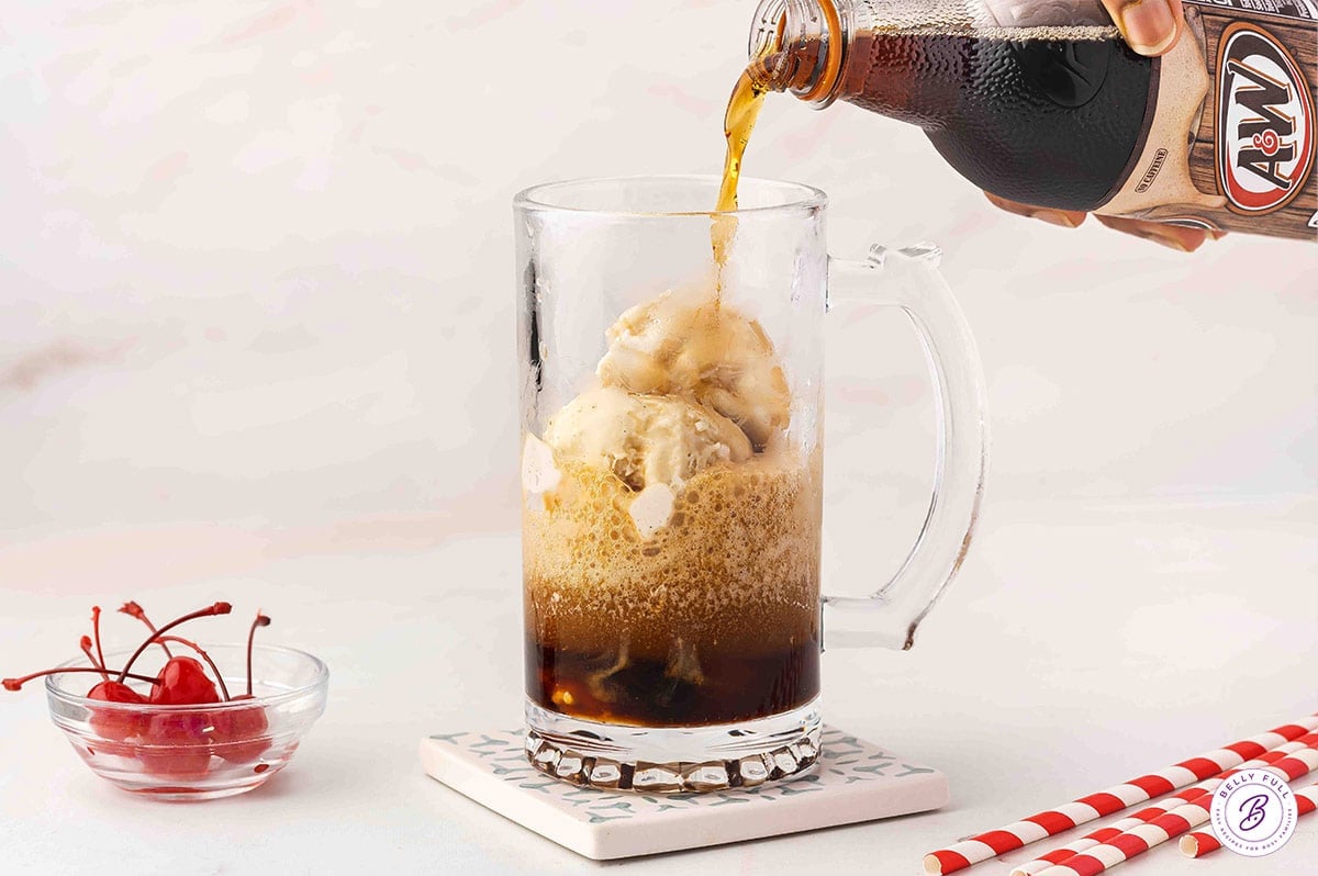 Pouring root beer over scoops of ice cream in a mug