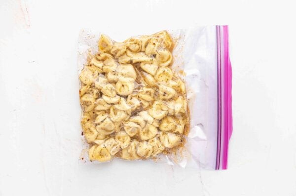 cooked tortellini with vinaigrette marinating in clear plastic bag