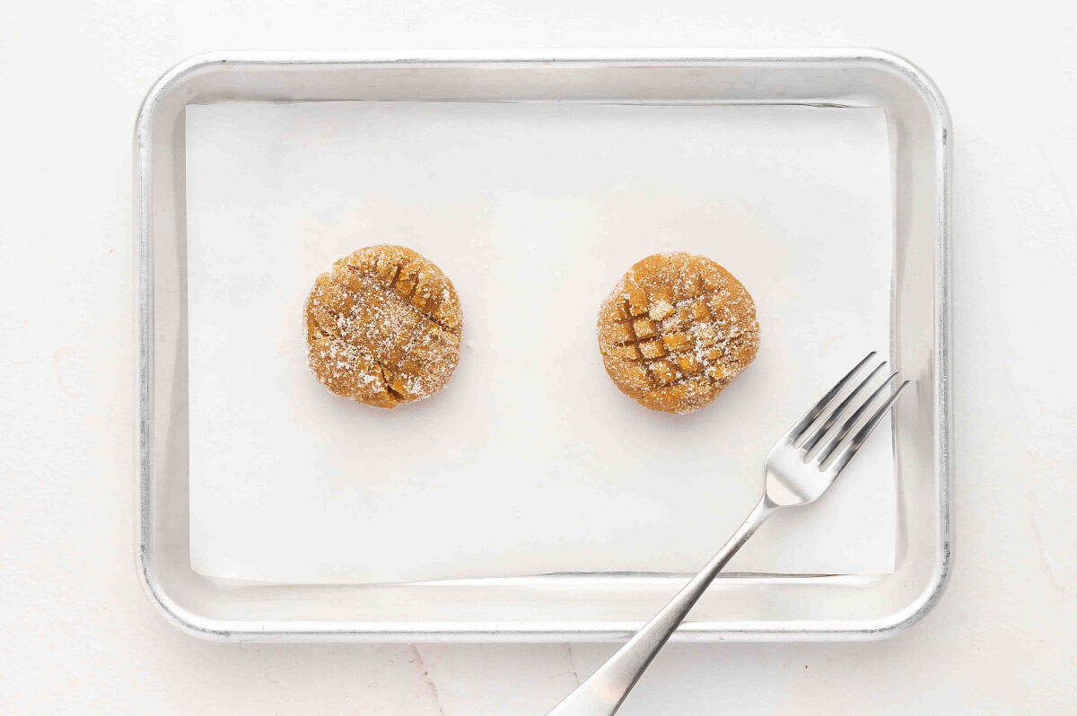 Two balls of peanut butter cookie dough on a baking sheet with a fork