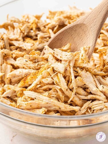 A wooden spoon stirring shredded chicken in a bowl