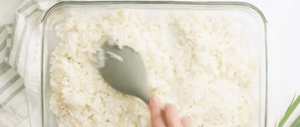 Patting down the cooked rice in a glass baking dish.