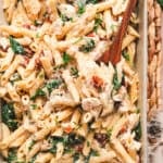 A wooden spoon in a casserole dish of baked Tuscan chicken pasta