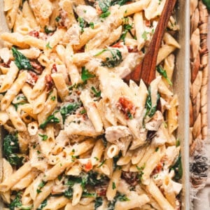 A wooden spoon in a casserole dish of baked Tuscan chicken pasta