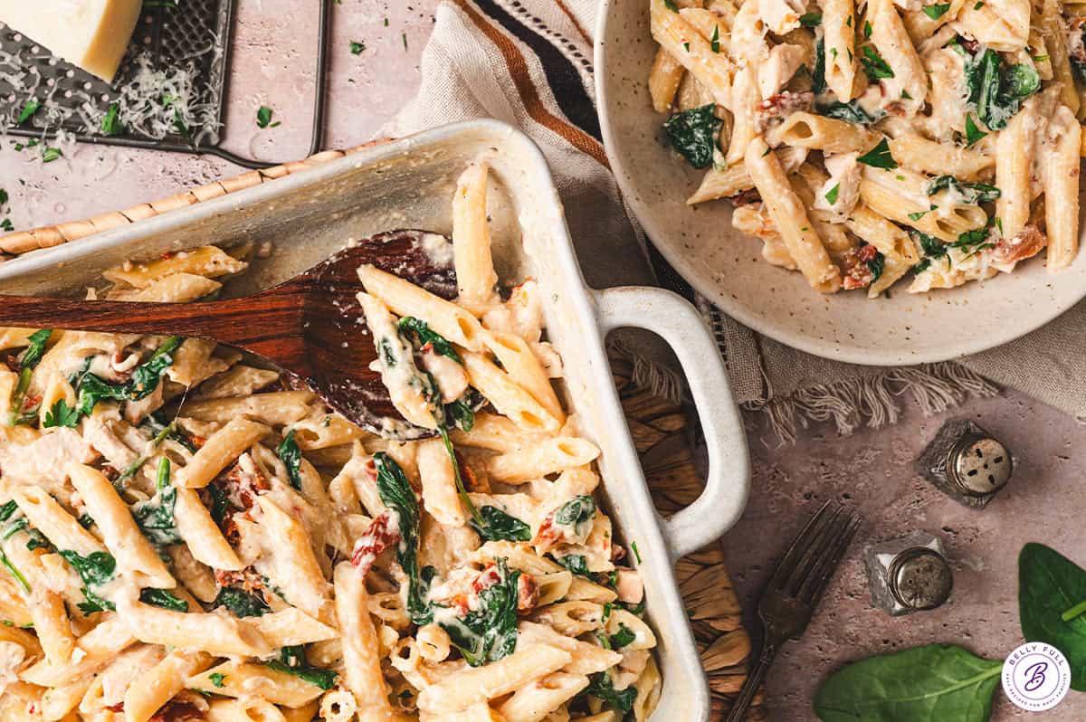 With penne pasta, spinach, and chicken tossed in a creamy sundried tomato sauce, this Baked Tuscan Chicken Pasta is an easy weeknight dinner. Overhead view of a baking dish and a plate of baked Tuscan chicken pasta