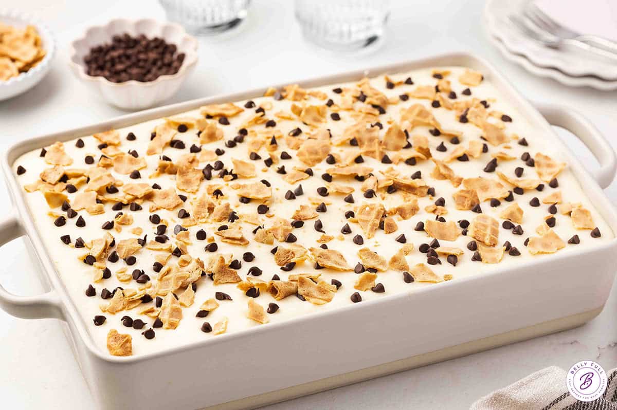 A vanilla poke cake is topped with a mascarpone ricotta frosting and mini chocolate chips in this easy Cannoli Cake recipe. Overhead view of a cannoli cake