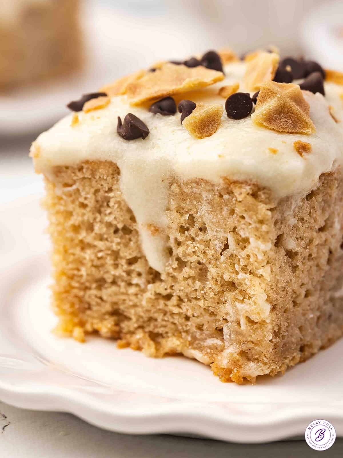 A vanilla poke cake is topped with a mascarpone ricotta frosting and mini chocolate chips in this easy Cannoli Cake recipe. A slice of cannoli cake on a white plate