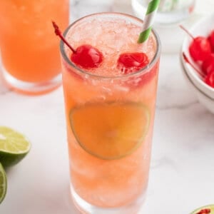 cherry limeade in glass with straw and sliced limes