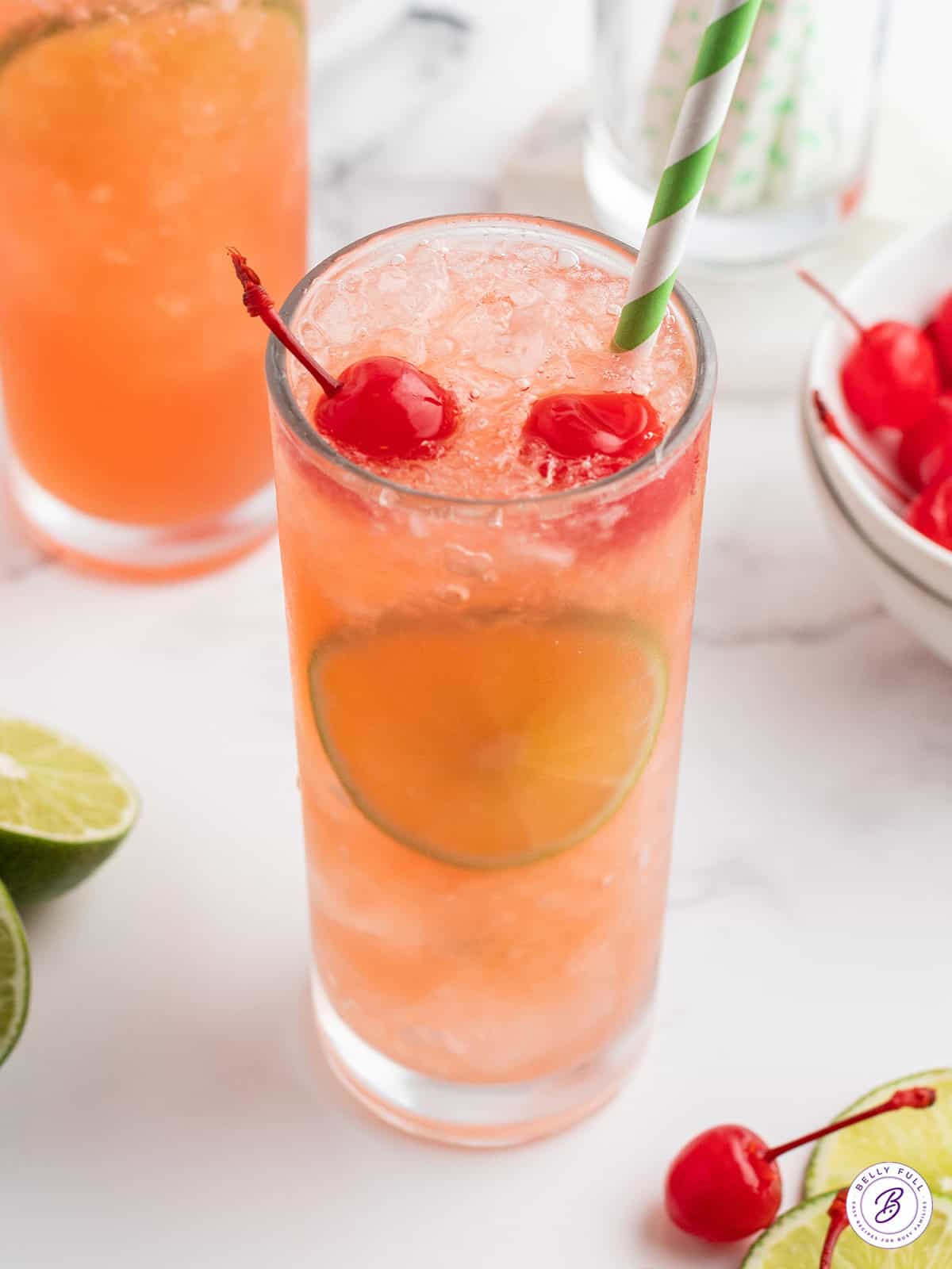 cherry limeade in glass with straw and sliced limes