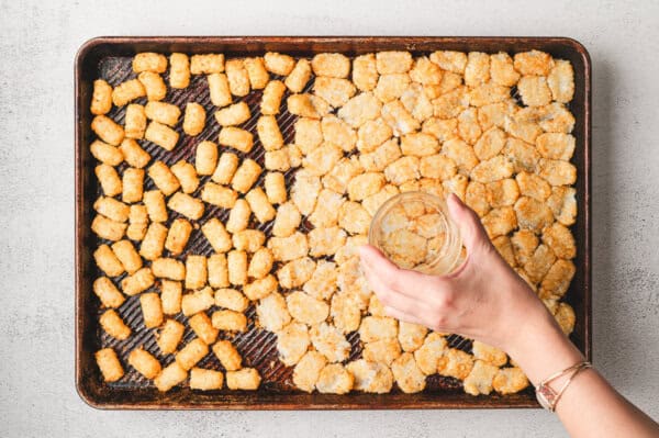 Smashing tater tots on a baking sheet with a wooden spoon